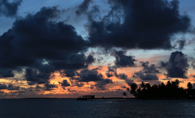 看那东边的天空，浓浓的云正堆积、游走，天空一点点 火红着，将哈达哈岛沙滩上的椰子树也披上了金光。而这时西边天空依然青蓝色，只是在栈桥的衔接处，那些红慢慢被晕染过去。